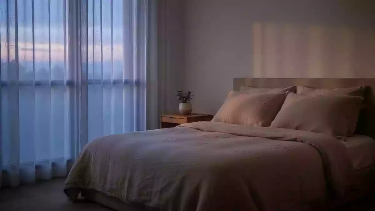 Ein ruhiges, minimalistisch eingerichtetes Schlafzimmer mit neutraler Bettwäsche und sanftem Tageslicht, das eine Atmosphäre der Erholung vermittelt. Illustration mit AI erstellt.