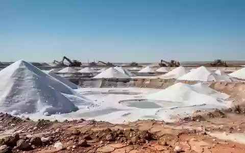 Weitläufiges Salzgewinnungsgelände mit großen Salzhalden und Baumaschinen unter blauem Himmel. - Foto: über boerse-global.de