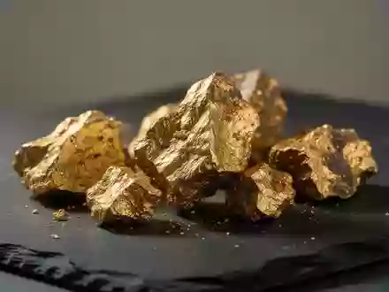 Rohgoldstücke auf einer dunklen, texturierten Oberfläche in einer professionellen Bergbauumgebung. - Foto: über boerse-global.de