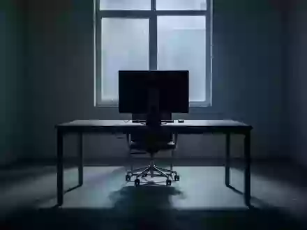 Ein unbesetzter, schattiger Arbeitsplatz in einem minimalistischen Büro mit einem ausgeschalteten Computerbildschirm. - Foto: über boerse-global.de