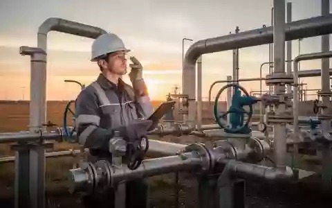 Techniker bei der Inspektion von Industrieanlagen zur Methan-Extraktion auf einem Feld bei Sonnenuntergang. - Foto: über boerse-global.de