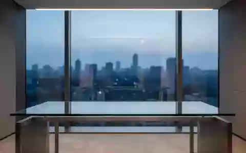 Ein minimalistischer, leerer Schreibtisch vor einem Fenster mit Blick auf eine Stadt bei Dämmerung. - Foto: über boerse-global.de
