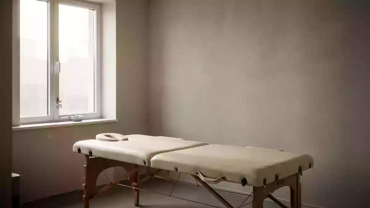 Ein minimalistischer, heller Behandlungsraum in einer Praxis mit einer Massageliege und sanftem Tageslicht. Illustration mit AI erstellt.