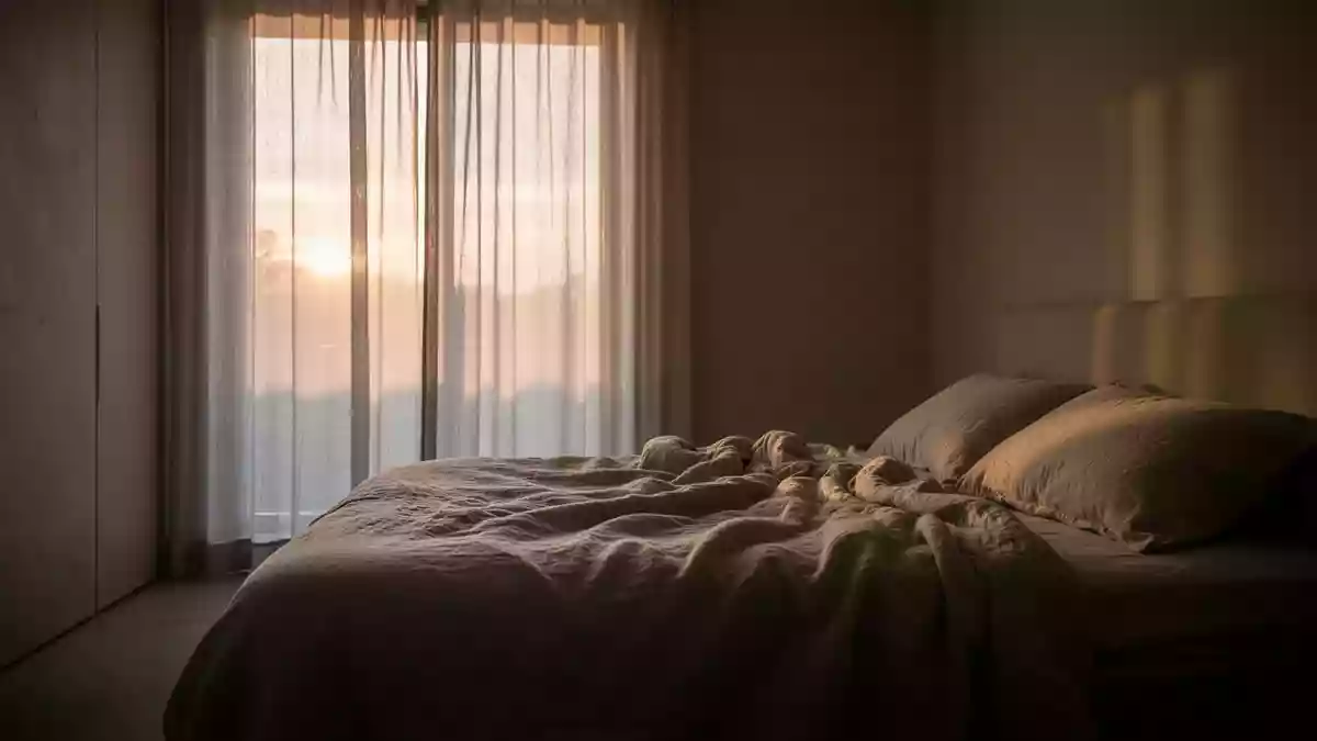 Ein minimalistisch eingerichtetes Schlafzimmer in der Morgendämmerung mit weichem Licht und einem ungemachten Bett. Illustration mit AI erstellt.