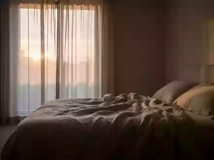 Ein minimalistisch eingerichtetes Schlafzimmer in der Morgendämmerung mit weichem Licht und einem ungemachten Bett. - Foto: über boerse-global.de