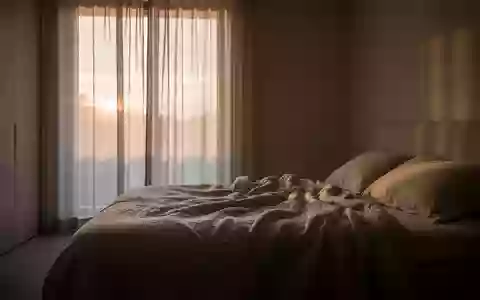 Ein minimalistisch eingerichtetes Schlafzimmer in der Morgendämmerung mit weichem Licht und einem ungemachten Bett. - Foto: über boerse-global.de