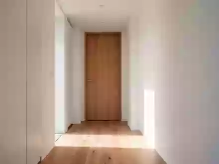 Ein heller, minimalistischer Flur in einem Wohngebäude mit Holzboden und einer geschlossenen Zimmertür. - Foto: über boerse-global.de