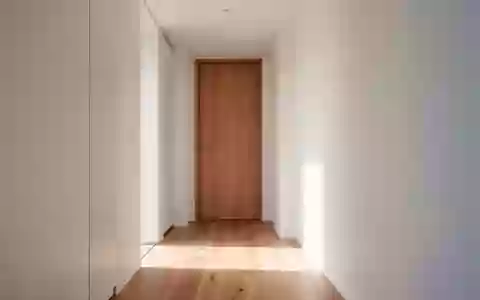 Ein heller, minimalistischer Flur in einem Wohngebäude mit Holzboden und einer geschlossenen Zimmertür. - Foto: über boerse-global.de