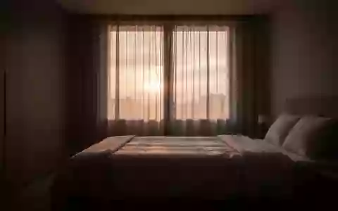 Ein minimalistisch eingerichtetes, in sanftes Morgenlicht getauchtes Schlafzimmer bei Sonnenaufgang. - Foto: über boerse-global.de