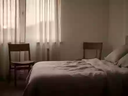 Ein ruhiges, minimalistisches Schlafzimmer im sanften Licht der Morgendämmerung mit einem leeren Stuhl am Fenster. - Foto: über boerse-global.de