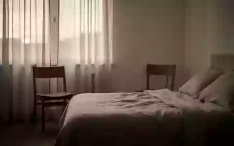 Ein ruhiges, minimalistisches Schlafzimmer im sanften Licht der Morgendämmerung mit einem leeren Stuhl am Fenster. - Foto: über boerse-global.de