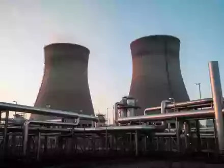 Moderne Industrieanlage mit großen Kühltürmen und Metallrohren bei Sonnenaufgang. - Foto: über boerse-global.de