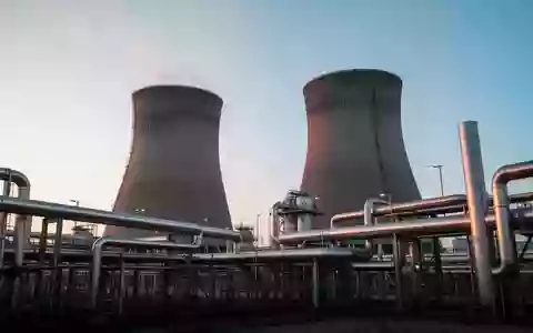 Moderne Industrieanlage mit großen Kühltürmen und Metallrohren bei Sonnenaufgang. - Foto: über boerse-global.de