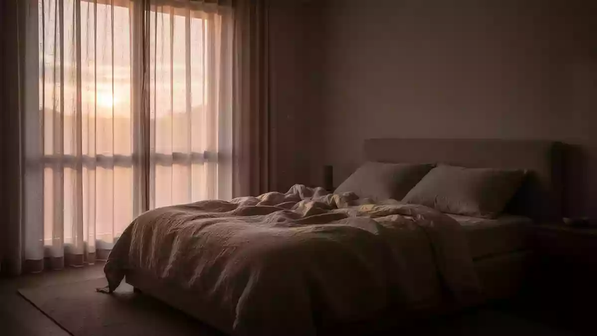 Ein ungemachtes Bett in einem ruhig beleuchteten Schlafzimmer am frühen Morgen. Illustration mit AI erstellt.