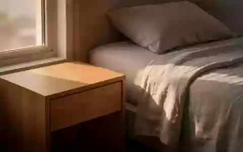 Ein minimalistischer Nachttisch in einem hellen, ruhigen Schlafzimmer bei Sonnenaufgang mit weichem Licht auf dem Bett. - Foto: über boerse-global.de