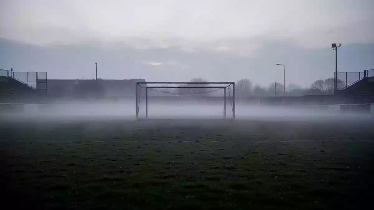 Ein leeres, nebliges Fußballfeld in der Dämmerung mit einem metallenen Torpfosten im Hintergrund. Illustration mit AI erstellt.