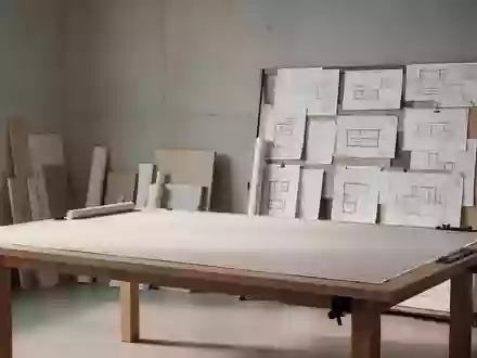 Ein minimalistischer, heller Design-Arbeitsbereich mit einem leeren Zeichentisch und Architekturplänen an einer Betonwand. - Foto: über boerse-global.de