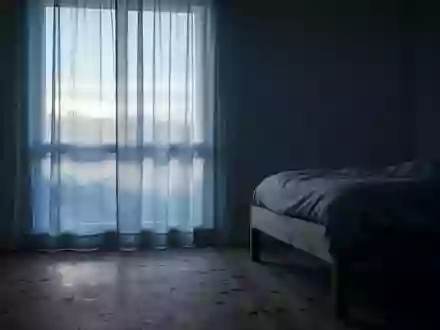 Ein minimalistisches Schlafzimmer bei Tagesanbruch, in dem sanftes Morgenlicht durch einen Vorhang auf den Boden fällt. - Foto: über boerse-global.de