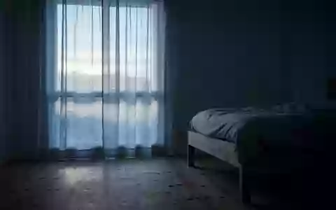 Ein minimalistisches Schlafzimmer bei Tagesanbruch, in dem sanftes Morgenlicht durch einen Vorhang auf den Boden fällt. - Foto: über boerse-global.de