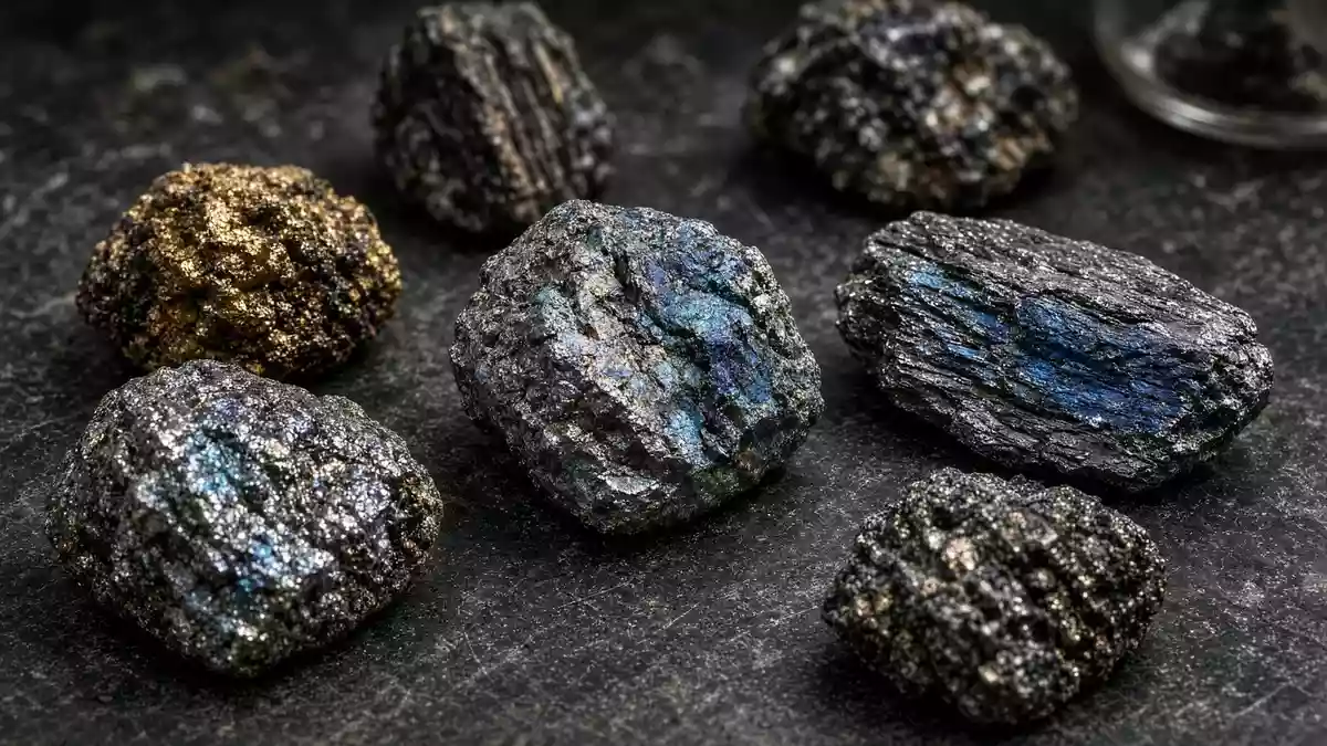 Nahaufnahme von verschiedenen, metallisch glänzenden Seltenerd-Mineralproben auf einem dunklen Labortisch. Illustration mit AI erstellt.