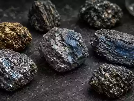 Nahaufnahme von verschiedenen, metallisch glänzenden Seltenerd-Mineralproben auf einem dunklen Labortisch. - Foto: über boerse-global.de