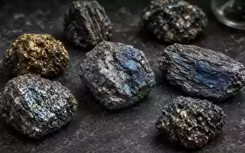 Nahaufnahme von verschiedenen, metallisch glänzenden Seltenerd-Mineralproben auf einem dunklen Labortisch. - Foto: über boerse-global.de