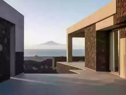 Eine moderne Architekturfassade aus Vulkangestein vor einer weitläufigen Küstenlandschaft auf Teneriffa bei Morgenlicht. - Foto: über boerse-global.de