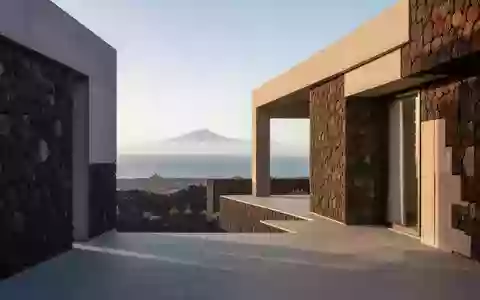 Eine moderne Architekturfassade aus Vulkangestein vor einer weitläufigen Küstenlandschaft auf Teneriffa bei Morgenlicht. - Foto: über boerse-global.de