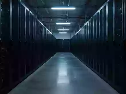 Ein langer, menschenleerer Gang in einem Rechenzentrum mit hoch aufragenden, dunklen Server-Racks in kühler Beleuchtung. - Foto: über boerse-global.de