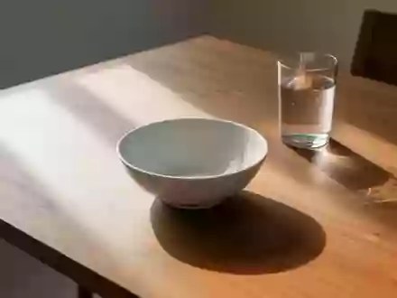 Ein leerer weißer Keramikteller und ein Glas Wasser auf einem hölzernen Esstisch im natürlichen Morgenlicht. - Foto: über boerse-global.de