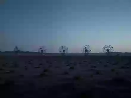 Eine weitläufige Wüstenlandschaft bei Dämmerung mit silhouettierten Satellitenantennen am Horizont. - Foto: über boerse-global.de