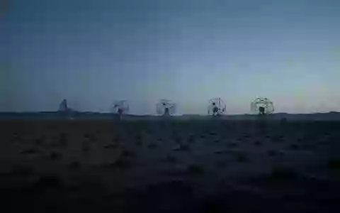 Eine weitläufige Wüstenlandschaft bei Dämmerung mit silhouettierten Satellitenantennen am Horizont. - Foto: über boerse-global.de
