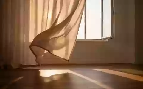 Ein ruhiger, minimalistischer Raum mit weichen, im Wind wehenden Leinenvorhängen und sanftem Sonnenlicht auf einem Holzboden. - Foto: über boerse-global.de