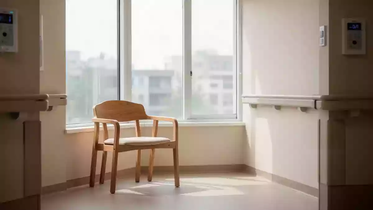 Ein ruhiger Bereich in einer Pflegeeinrichtung mit einem leeren Holzstuhl vor einem hellen Fenster. Illustration mit AI erstellt.