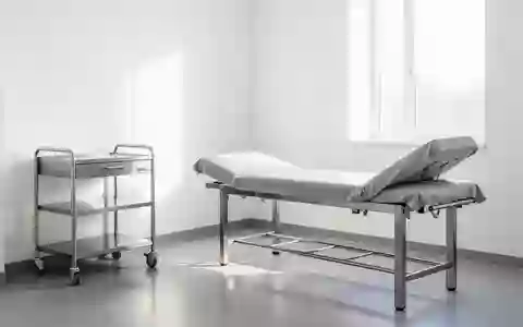 Ein heller, minimalistischer Behandlungsraum in einer Klinik mit einer Untersuchungsliege und einem medizinischen Wagen. - Foto: über boerse-global.de