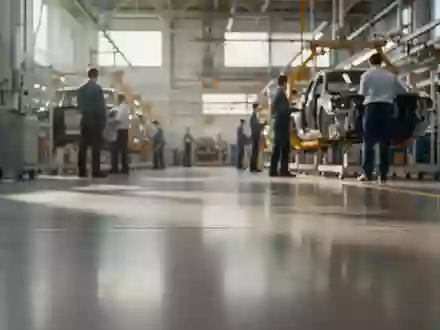 Moderne Fertigungshalle in einem Automobilwerk mit unscharfen Mitarbeitern im Hintergrund. - Foto: über boerse-global.de
