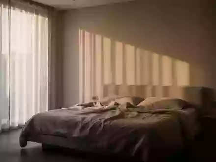 Ein minimalistisch eingerichtetes Schlafzimmer am frühen Morgen mit sanftem, durch Vorhänge einfallendem Tageslicht. - Foto: über boerse-global.de