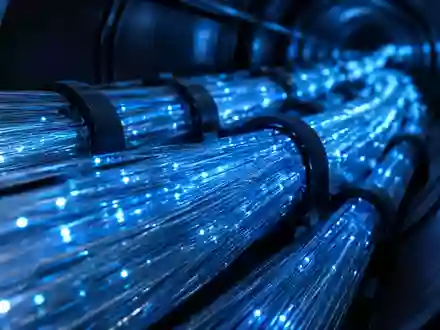 Nahaufnahme eines komplexen Glasfaserkabelnetzes mit blauem Licht in einem dunklen, industriellen Leitungsschacht. - Foto: über boerse-global.de