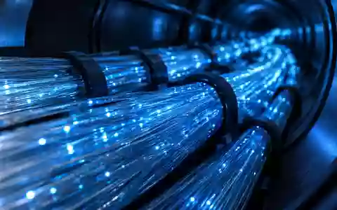 Nahaufnahme eines komplexen Glasfaserkabelnetzes mit blauem Licht in einem dunklen, industriellen Leitungsschacht. - Foto: über boerse-global.de