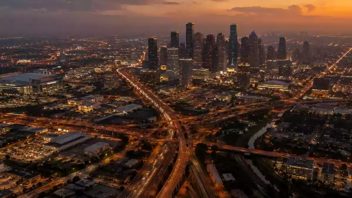 Ein weitläufiger Blick aus der Vogelperspektive auf das nächtliche Straßennetz von Houston, Texas, bei Dämmerung. Illustration mit AI erstellt.