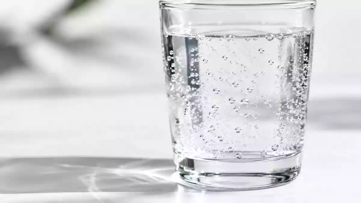 Ein klares Glas mit sprudelndem Wasser auf einem minimalistischen weißen Untergrund. Illustration mit AI erstellt.