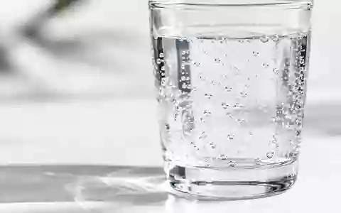 Ein klares Glas mit sprudelndem Wasser auf einem minimalistischen weißen Untergrund. - Foto: über boerse-global.de