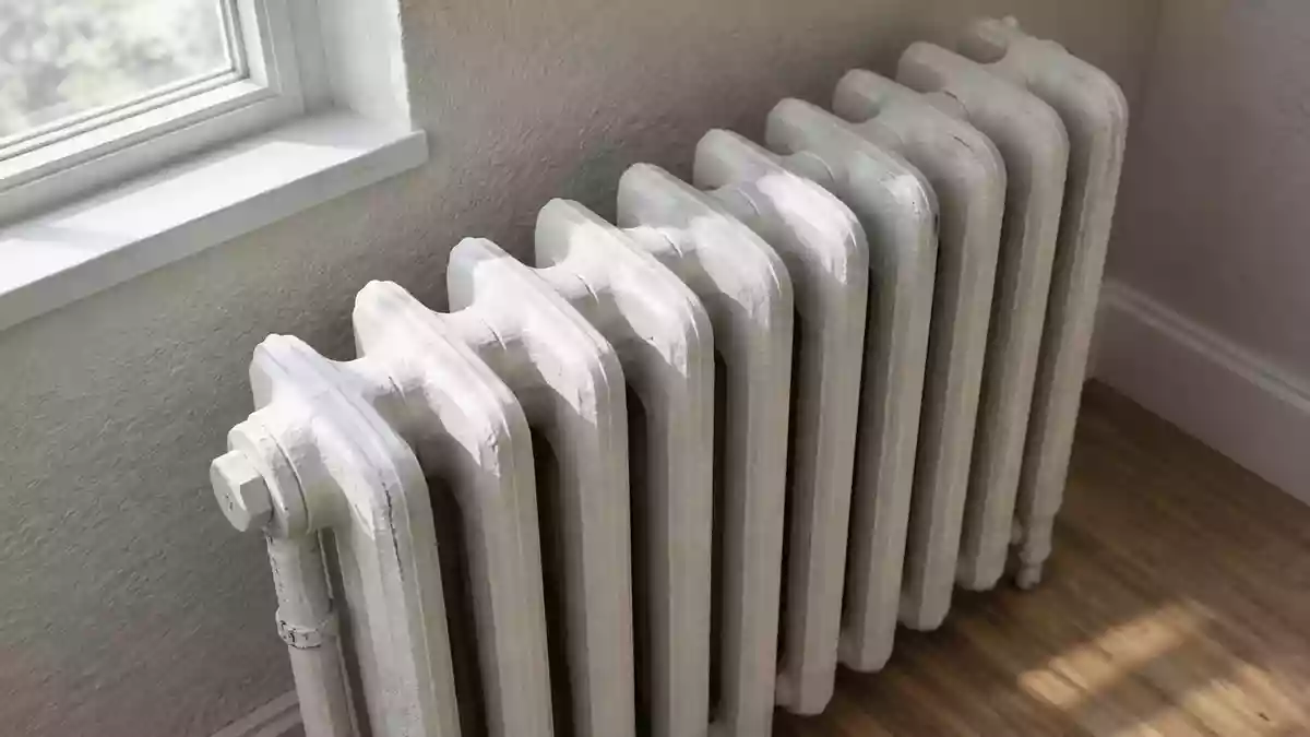 Ein weißer, gusseiserner Heizkörper an einer schlichten Wand in einem hellen, unbewohnten Zimmer. Illustration mit AI erstellt.