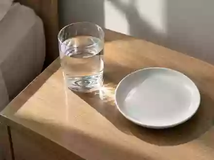 Ein Glas Wasser und ein leerer weißer Teller auf einem schlichten Holztisch bei natürlichem Morgenlicht. - Foto: über boerse-global.de