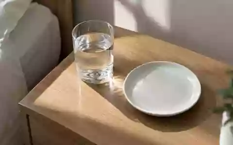 Ein Glas Wasser und ein leerer weißer Teller auf einem schlichten Holztisch bei natürlichem Morgenlicht. - Foto: über boerse-global.de