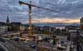 Baustelle in einer Schweizer Stadt mit einem Turmdrehkran vor einem bewölkten Himmel bei Dämmerung. - Foto: über boerse-global.de