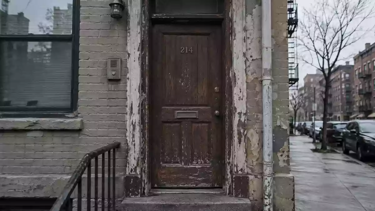 Eine verschlossene, abgenutzte Wohnungstür in einem städtischen Wohnviertel bei trübem Tageslicht. Illustration mit AI erstellt.