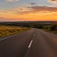 Eine leere, moderne Landstraße bei Sonnenuntergang mit deutlichen Fahrbahnmarkierungen in einer ländlichen Umgebung. - Foto: über boerse-global.de
