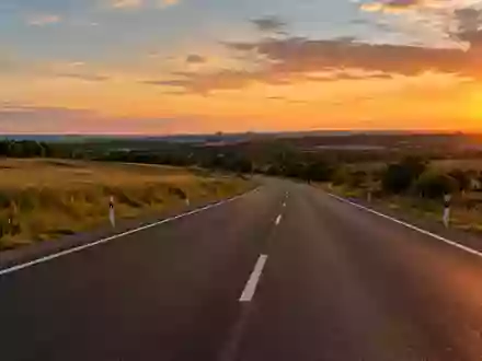 Eine leere, moderne Landstraße bei Sonnenuntergang mit deutlichen Fahrbahnmarkierungen in einer ländlichen Umgebung. - Foto: über boerse-global.de