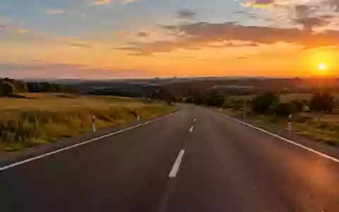 Eine leere, moderne Landstraße bei Sonnenuntergang mit deutlichen Fahrbahnmarkierungen in einer ländlichen Umgebung. - Foto: über boerse-global.de